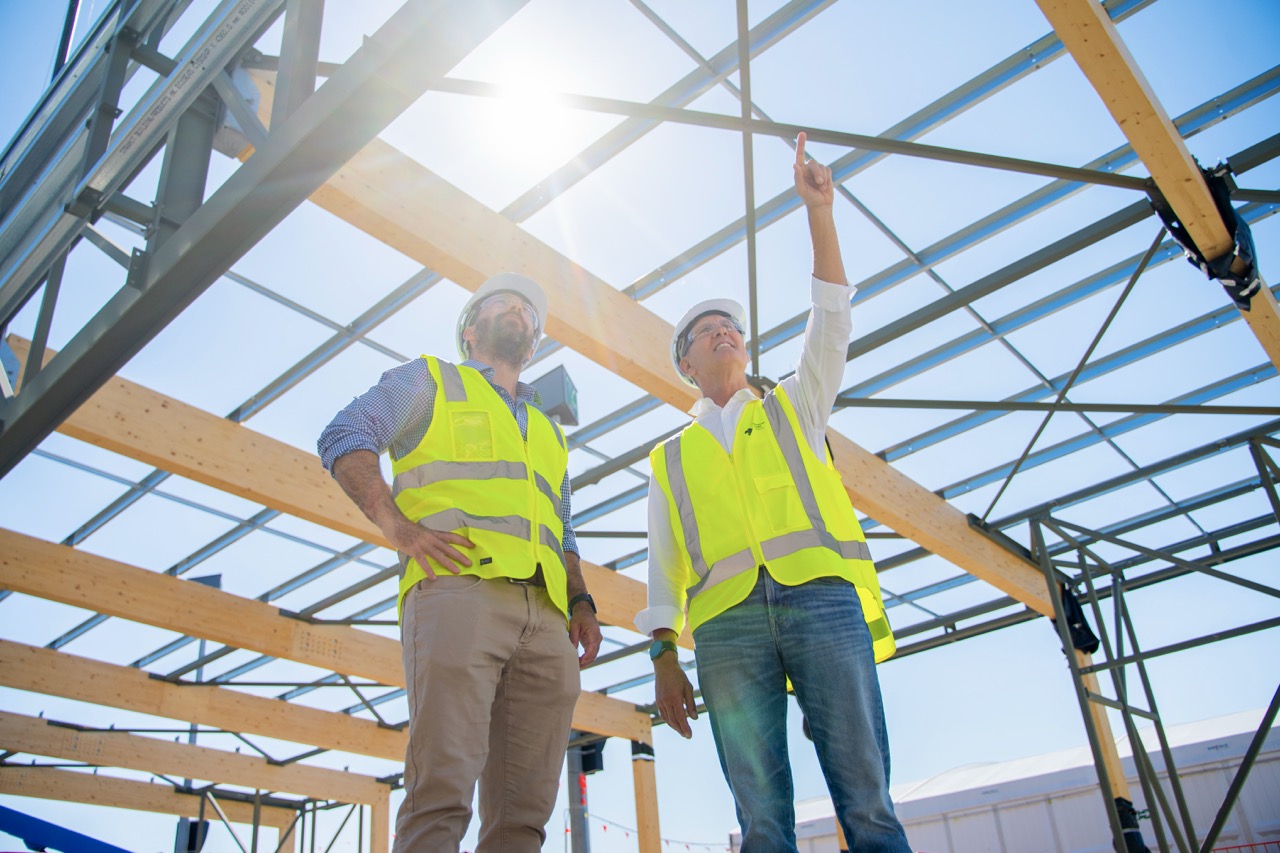 Two men in hi-vis vests inspect the steel and glulam roof structure of the new Sunshine Coast Airport terminal